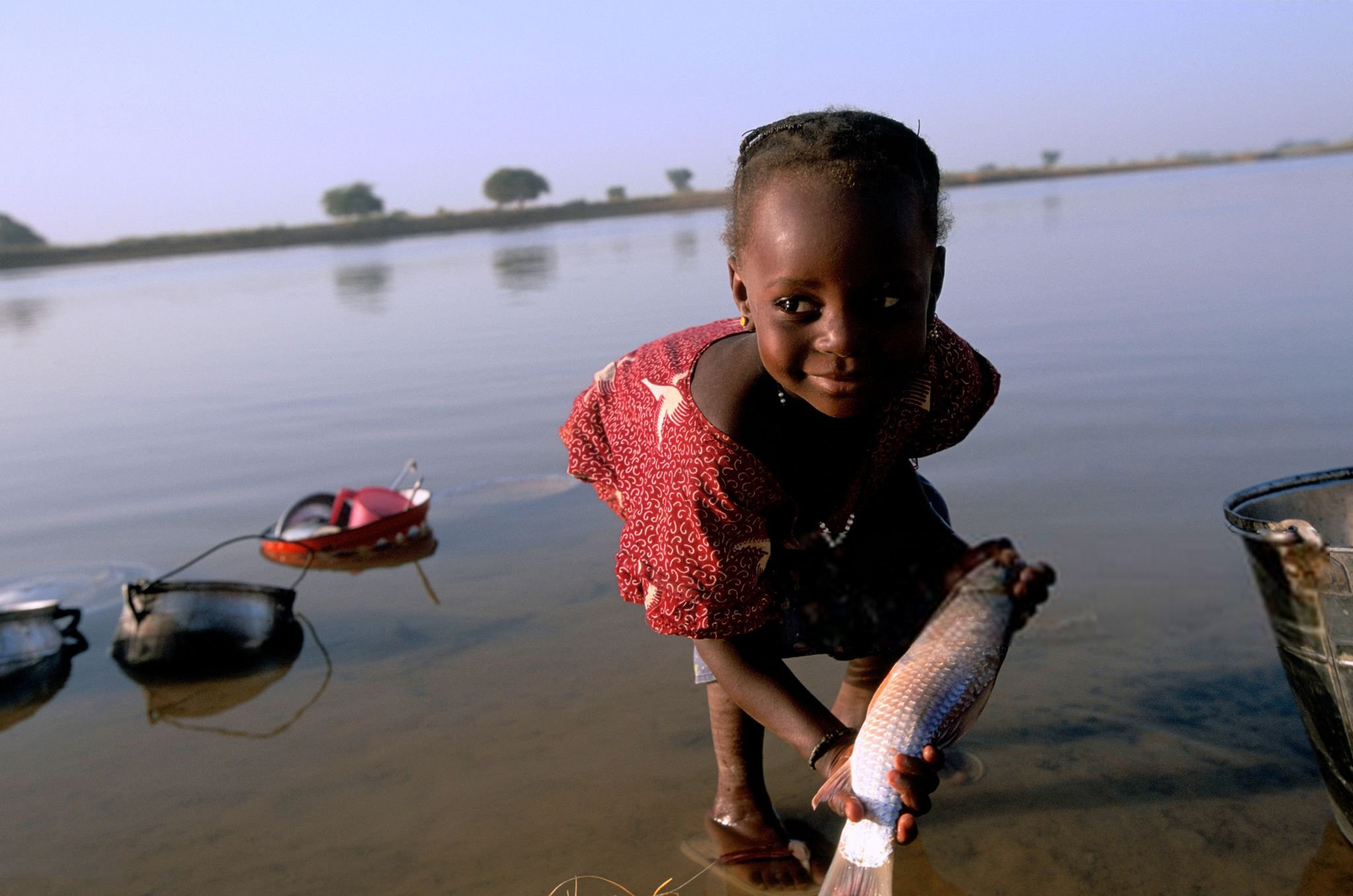 gettyimages-Veronique Durruty--little girl of Diafarabe in Niger A little girl of Diafarabe Fulani's village on the banks of the River Niger, cleans her clothes and a fish for lunch, Niger.