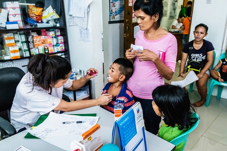 2019 A mother brings her children for check-up and vaccination at the Corazon Aquino Health Center in Baseco Compound, Tondo, Manila. All services are free at the health center.